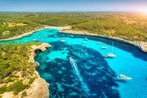 Vue aérienne d’une zone côtière avec des eaux turquoise limpides, des bateaux et un paysage rocheux.
