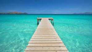 A wooden pier extending into clear turquoise water with a distant mountain range.
