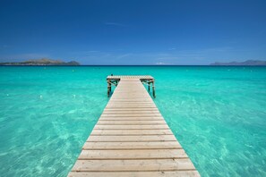 Une jetée en bois s’étendant dans une eau turquoise et limpide, avec une chaîne de montagnes visible au loin.