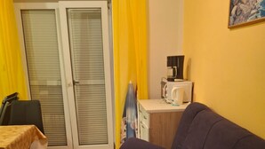 Una sala de estar con un sofá oscuro, una mesita con mantel amarillo, una silla y una zona de cocina con un microondas.