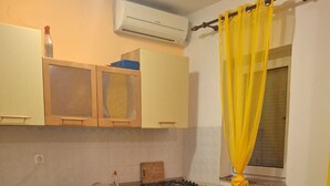 Cocina compacta con estufa a gas, pileta y alacenas de madera. Se aprecia una mesa de comedor con sillas y un cortin amarillo.