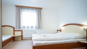 Et soveværelse med en træseng, et sengebord, en stol, et vindue med gardiner og en radiator.