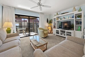 Un salon comprenant un ensemble de canapés, une table basse en verre, un téléviseur posé sur un meuble de télévision blanc, et un balcon avec vue.