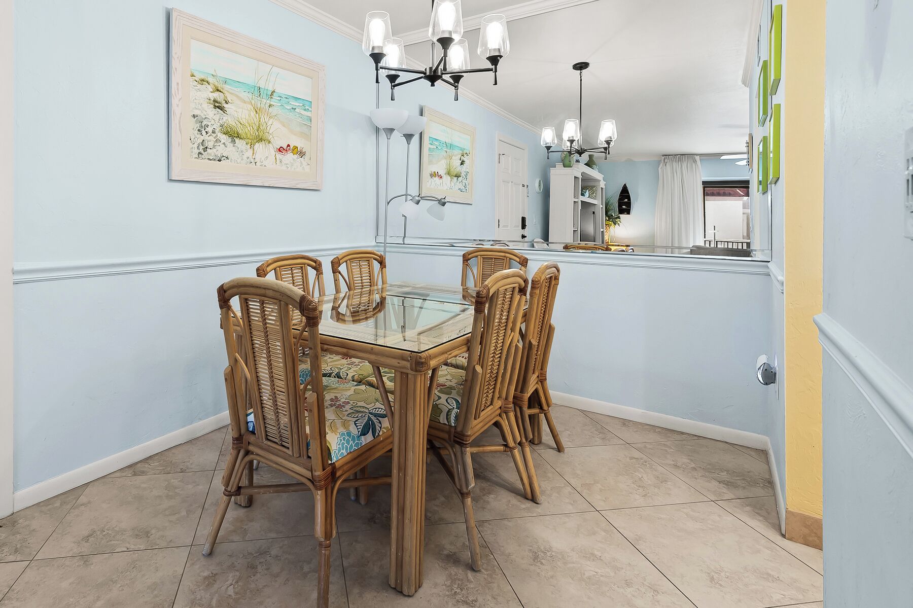 A dining area with a glass-top table surrounded by wicker chairs, light blue walls, and a ceiling with a chandelier.