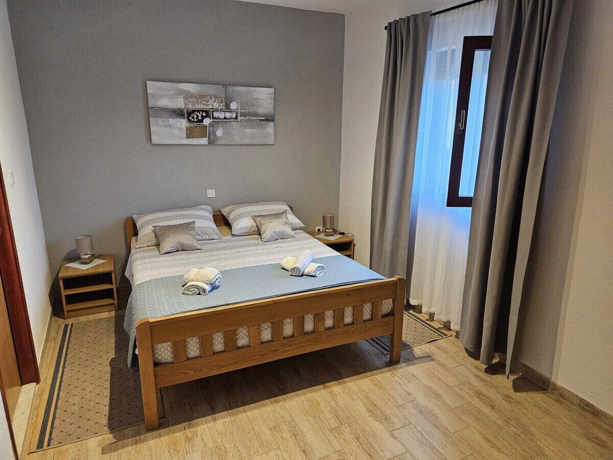 A neatly arranged bedroom with a wooden bed, a bedside table with a lamp, and a wall-mounted abstract art piece.