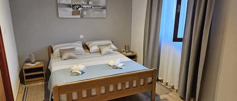 A neatly arranged bedroom with a wooden bed, a bedside table with a lamp, and a wall-mounted abstract art piece.