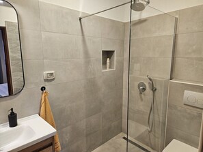 Une salle de bain moderne avec une douche à parois de verre, un lavabo doté d’un distributeur de savon et une serviette suspendue à un crochet.
