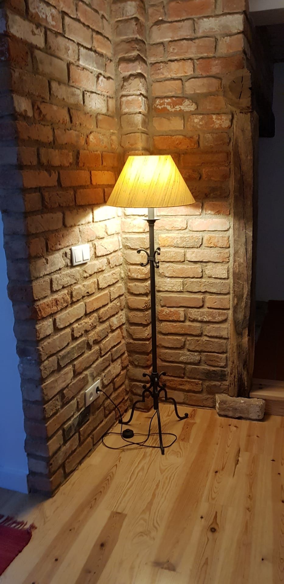 A corner lamp with a wooden shade against a brick wall.