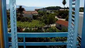 A view from a balcony with a blue railing, overlooking a residential area with houses, trees, and a clear sky. - Apartment in Sućuraj with Seaview, Balcony, Air condition, WIFI (3560-1) (Sucuraj)