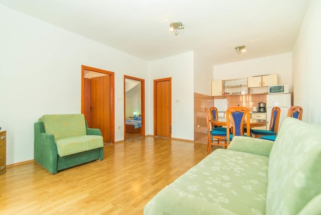 Ein geräumiger Wohnbereich mit Holzboden, einem grünen Sofa und einem Esstisch mit Stühlen.