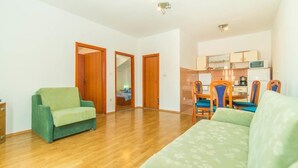 A spacious living area with a wooden floor, a green sofa, and a dining table with chairs.