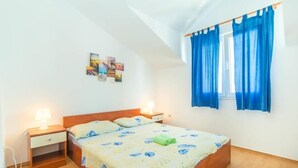 A single-bed room with a wooden headboard, a bedside table with a lamp, and a window with blue curtains.