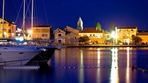 A marina with boats docked, a church with a bell tower, and residential buildings along the waterfront. - Apartment in Sukošan with Terrace, Air condition, WIFI (654-4) (Sukošan)
