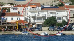 Ein Küstengebäude mit mehreren Balkonen, ein Restaurant mit Außenbereich und eine Marina mit Booten.