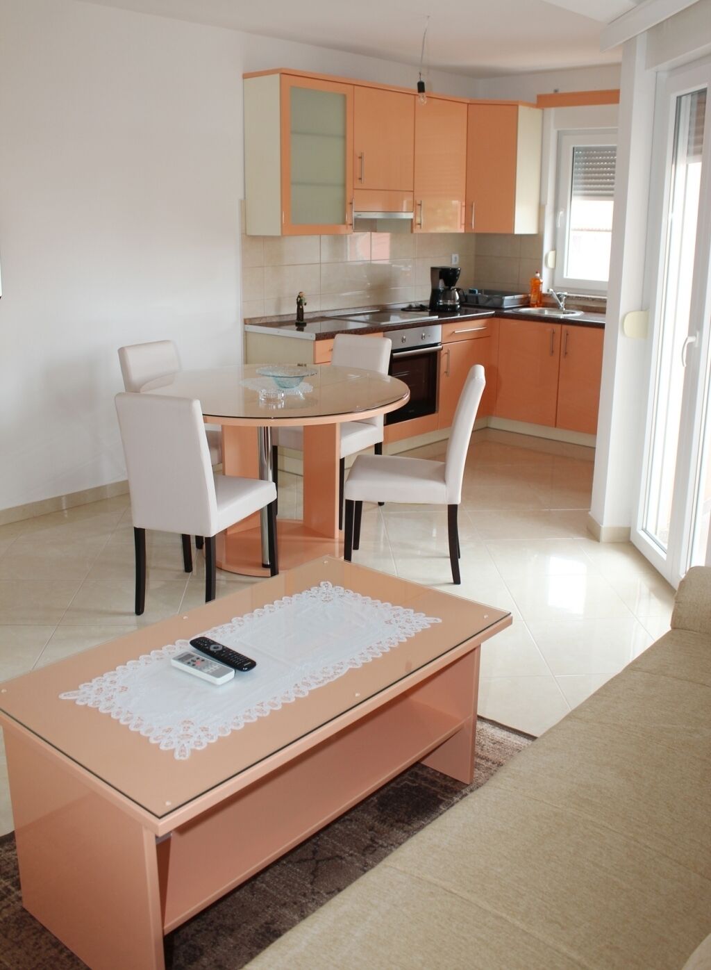 Een moderne keuken met oranje kastjes, een eettafel met stoelen en een koffieapparaat.