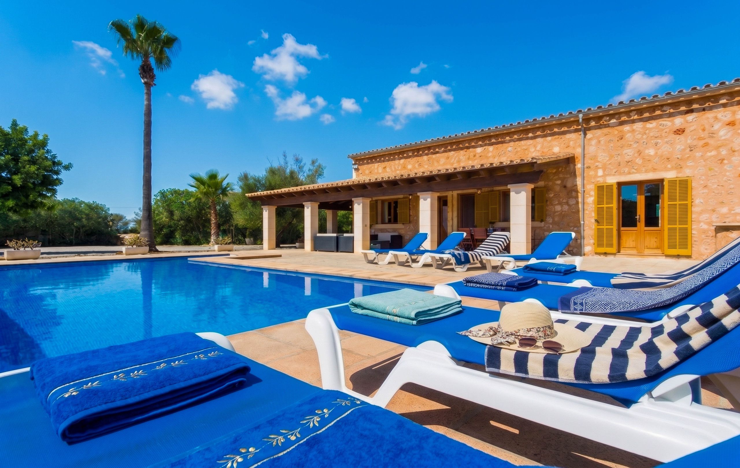 A poolside area with lounge chairs and a stone building with a tiled roof.