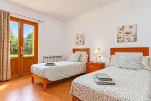 Quarto com duas camas, janela com cortinas, radiador e obras de arte nas paredes.
