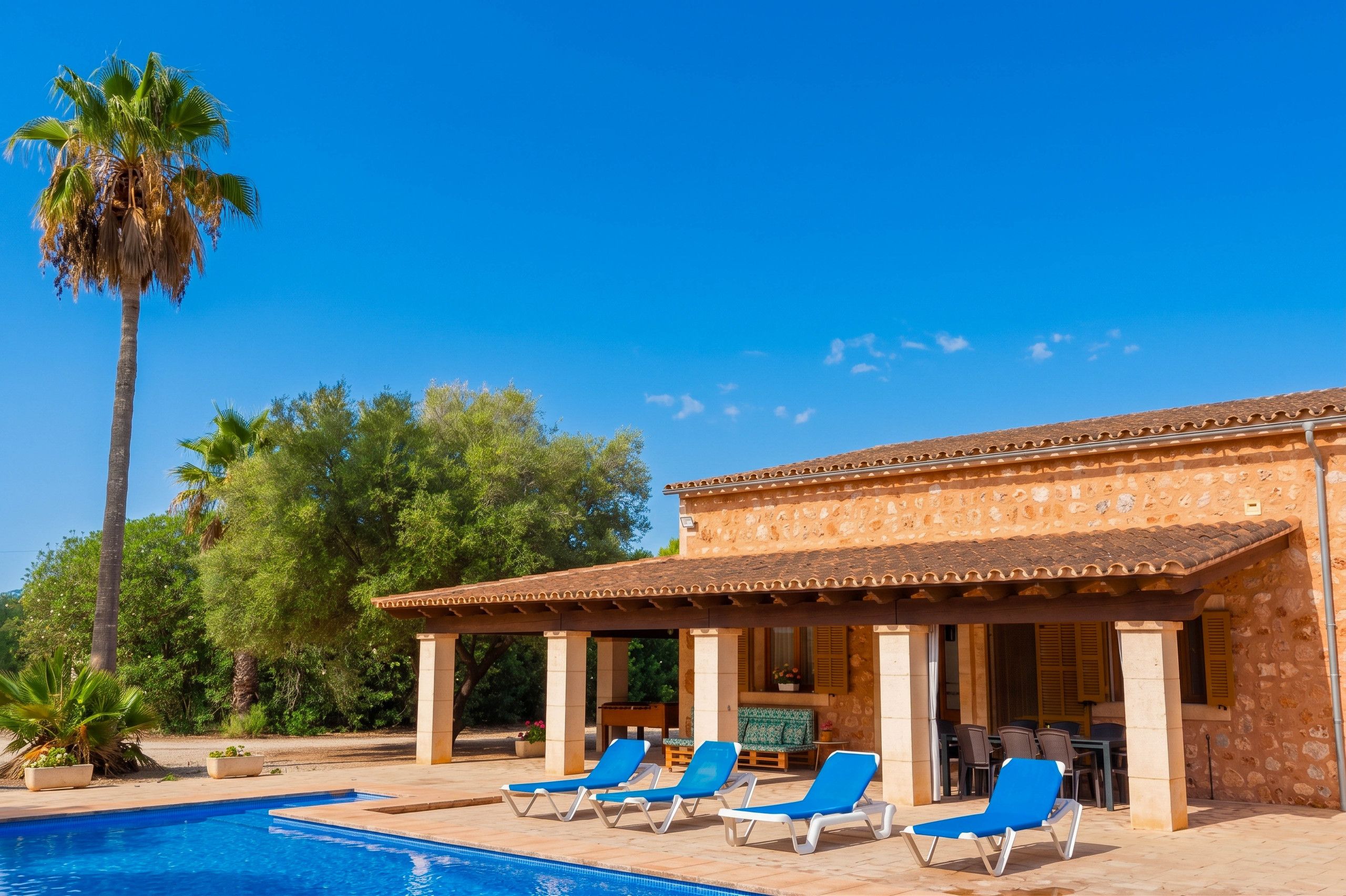 Un espace aménagé au bord de la piscine, avec des chaises longues et un bâtiment doté d’un toit recouvert de tuiles.