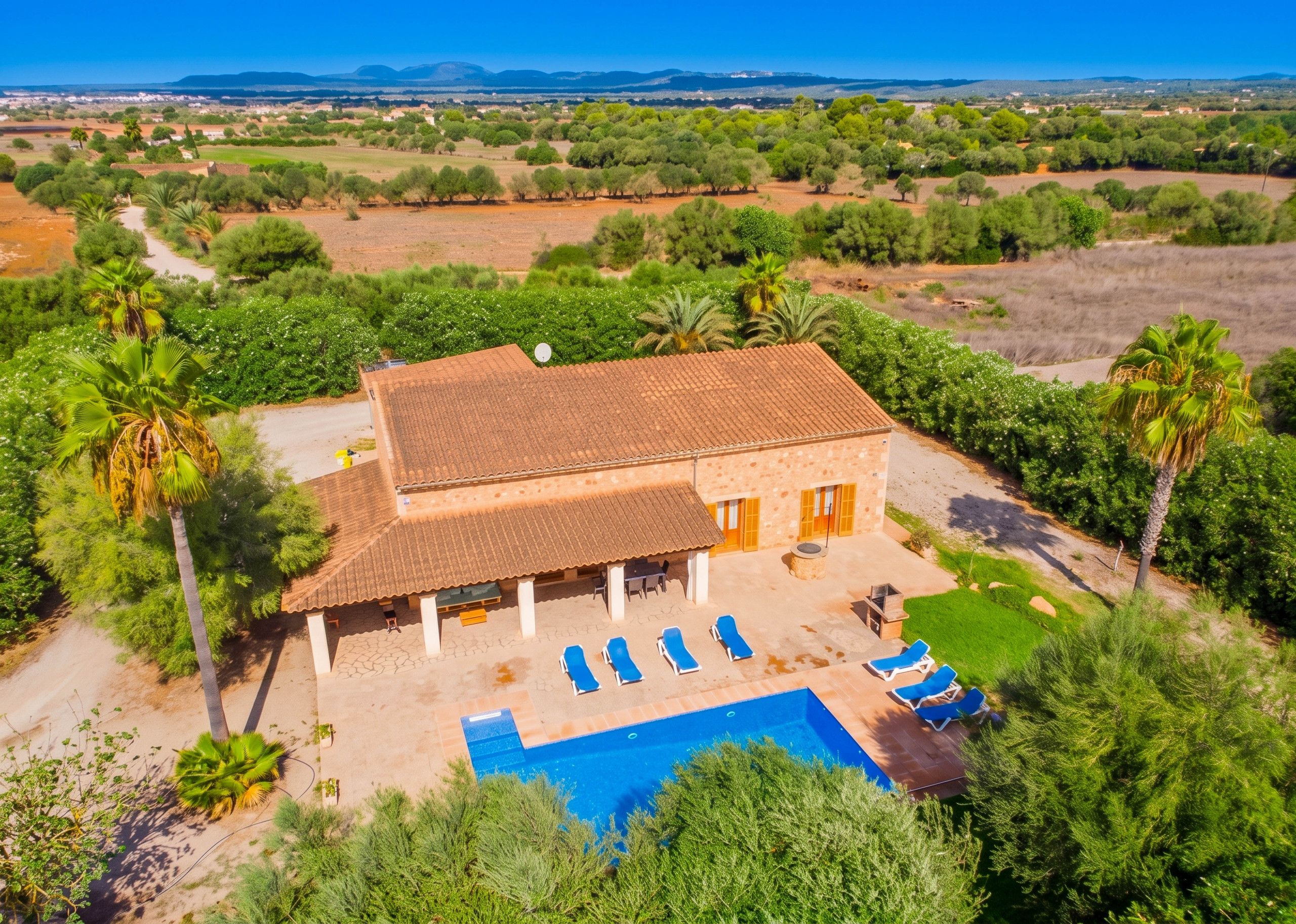 A two-story building with a swimming pool, outdoor seating, and a view of a rural landscape.