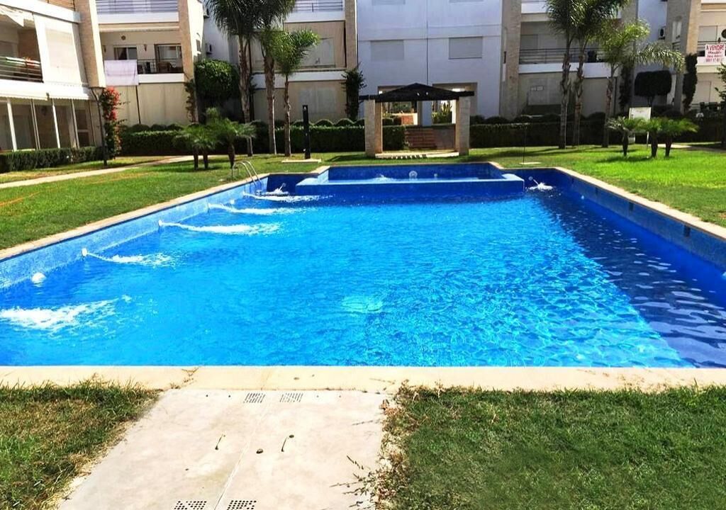 Una piscina rectangular con agua azul cristalina, rodeada de césped y un sendero pavimentado.