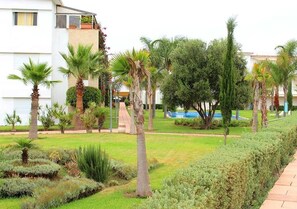 A landscaped garden with palm trees, a swimming pool, and a building with balconies.