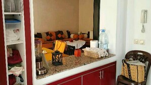 Un salon comprenant un canapé, une table basse et un coin cuisine avec un réfrigérateur et un évier.