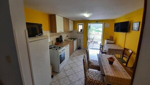 A compact kitchen with a stove, microwave, and cabinets. There is a dining area with a table and chairs, and a TV mounted on the wall.
