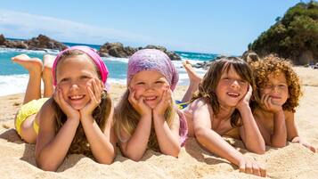 Children can play on the sandy beach with the ocean and rocky cliffs in the background.