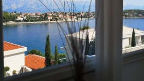 A view through a window with a vase of branches, overlooking a body of water, buildings, and mountains. - Holiday Home in Sumartin with Seaview, Air condition, WIFI, Washing machine (682-2) (Sumartin)
