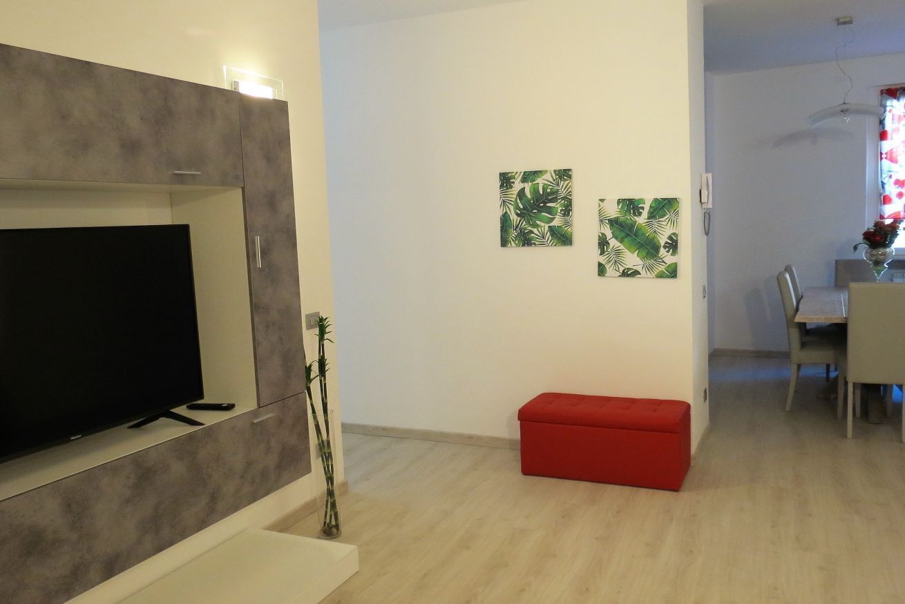 Ein modernes Wohnzimmer mit einem Flachbildfernseher, einem roten Hocker und zwei an der Wand befestigten Kunstwerken.