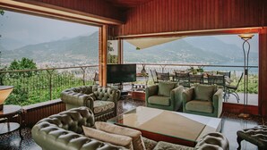 Amplia sala de estar con sofás de cuero, una mesa de centro de vidrio y un televisor. Cuenta con un ventanal con vistas a la ciudad y las montañas.