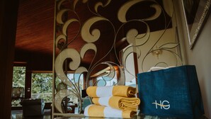 Habitación de hotel con una mesa de vidrio, un separador metálico decorativo y una bolsa azul con un logotipo.
