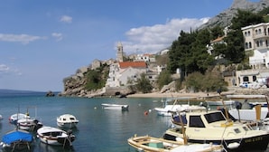A coastal town with boats docked at a marina, a prominent church with a bell tower, and buildings with red-tiled roofs.