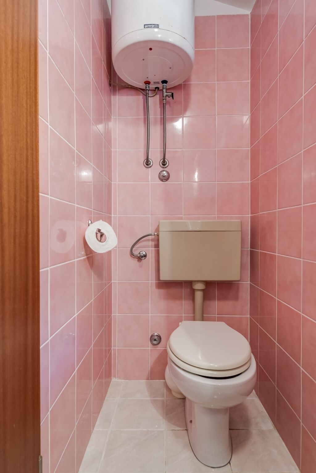 A bathroom with pink tiles, a toilet, a bidet, and a water heater.