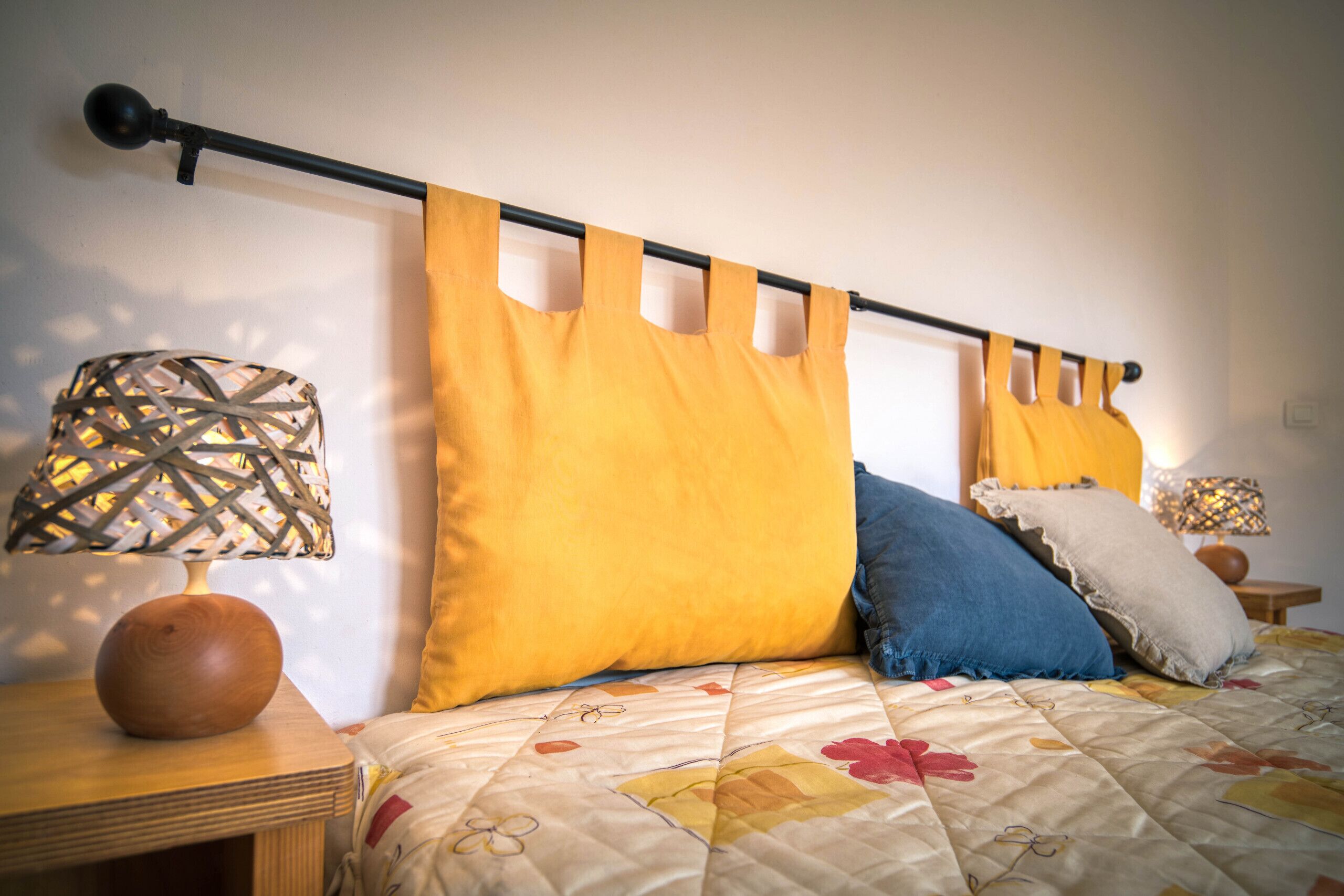 A bed with a floral quilt, a wooden nightstand with a lamp, and a headboard with cut-out panels.