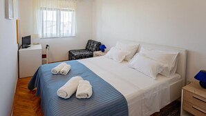 A hotel room with a bed, a desk with a computer, a chair, and a window with curtains.
