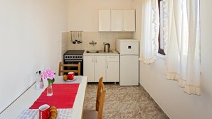 A compact kitchen with white cabinets, a stove, a sink, and a refrigerator. There's a dining table with a red placemat and a vase of flowers.