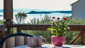 A balcony with a view of a lake and distant mountains, a pink flower pot, and a table with a mug. - Holiday Home in Drage with Seaview, Balcony, Air condition, WIFI (571-1) (Drage)