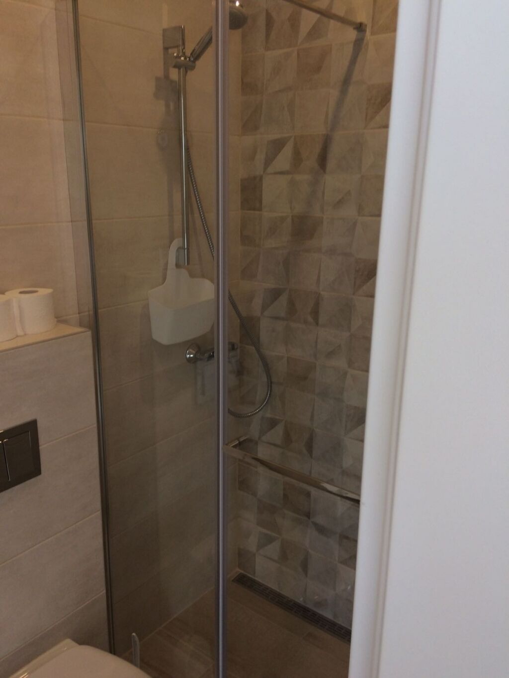 A glass-enclosed shower with a handheld showerhead and a wall-mounted faucet.