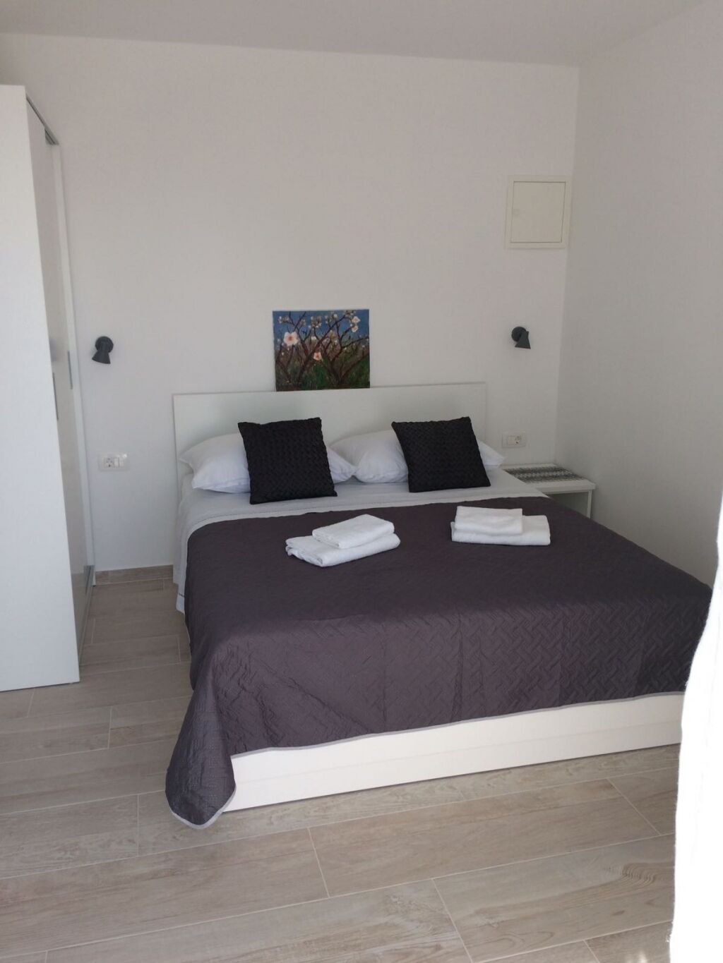 Un dormitorio con cama, almohadas, un cuadro en la pared y una mesita de noche.