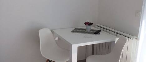 A small, white dining area with a table and two chairs, a radiator below, and a TV mounted on the wall.
