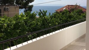 A balcony with a view of the sea, greenery, and a building with a red roof. - Studio apartment in Podgora with Seaview, Balcony, Air condition, WIFI (4492-4) (Podgora)