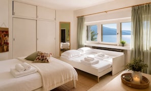 Ein Hotelzimmer mit zwei Betten, Meerblick, einem Vorhangfenster und einem Nachttisch mit Kerze.