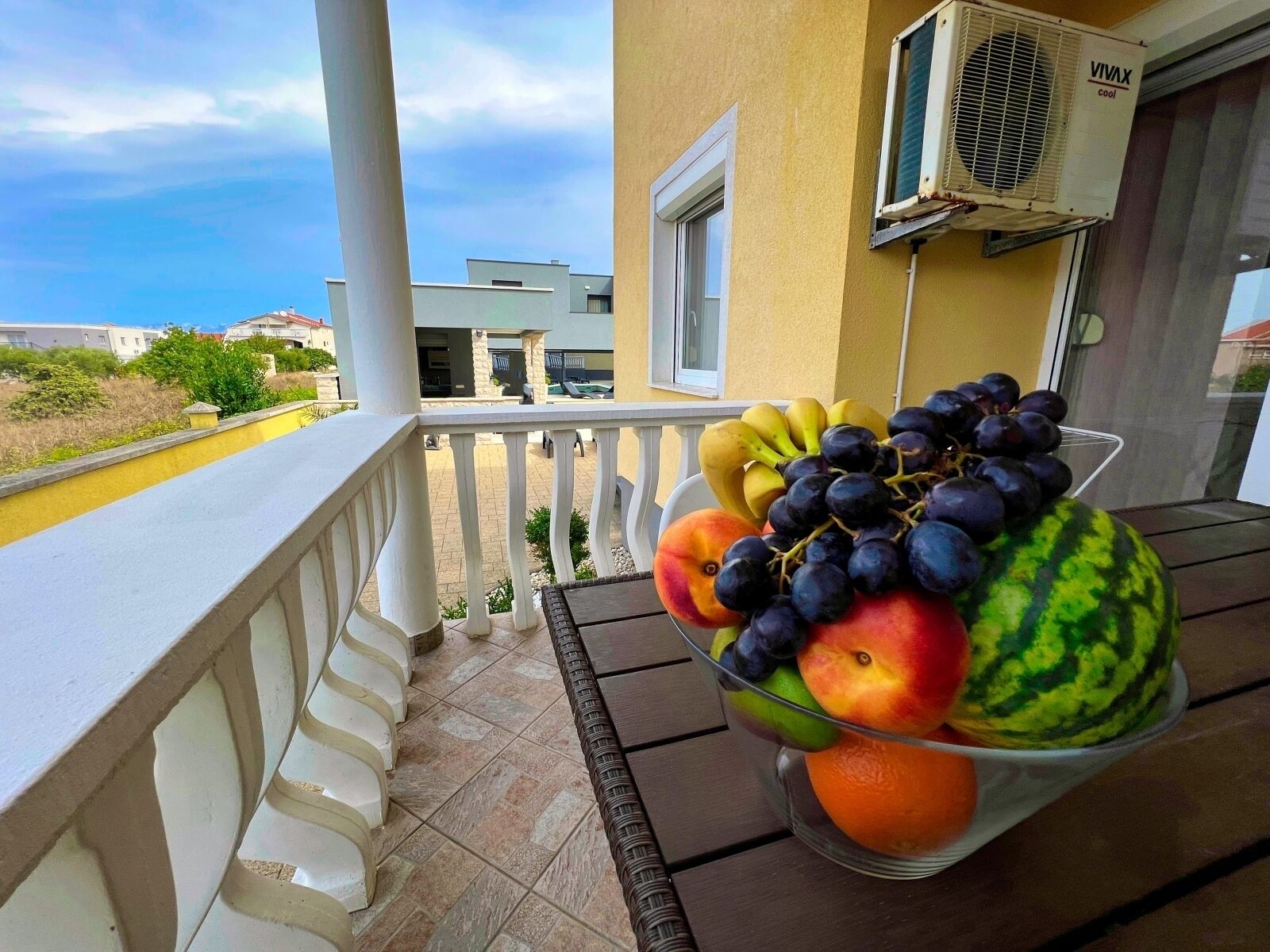 Un balcón con una cesta de frutas que contiene uvas, sandía, una manzana y plátanos.