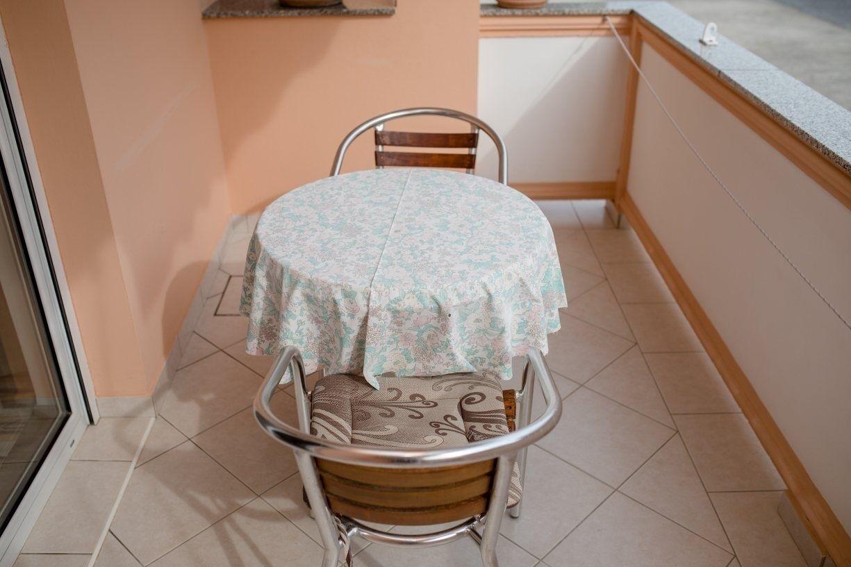 A small balcony with a round table and two chairs, a tiled floor, and a peach-colored wall.