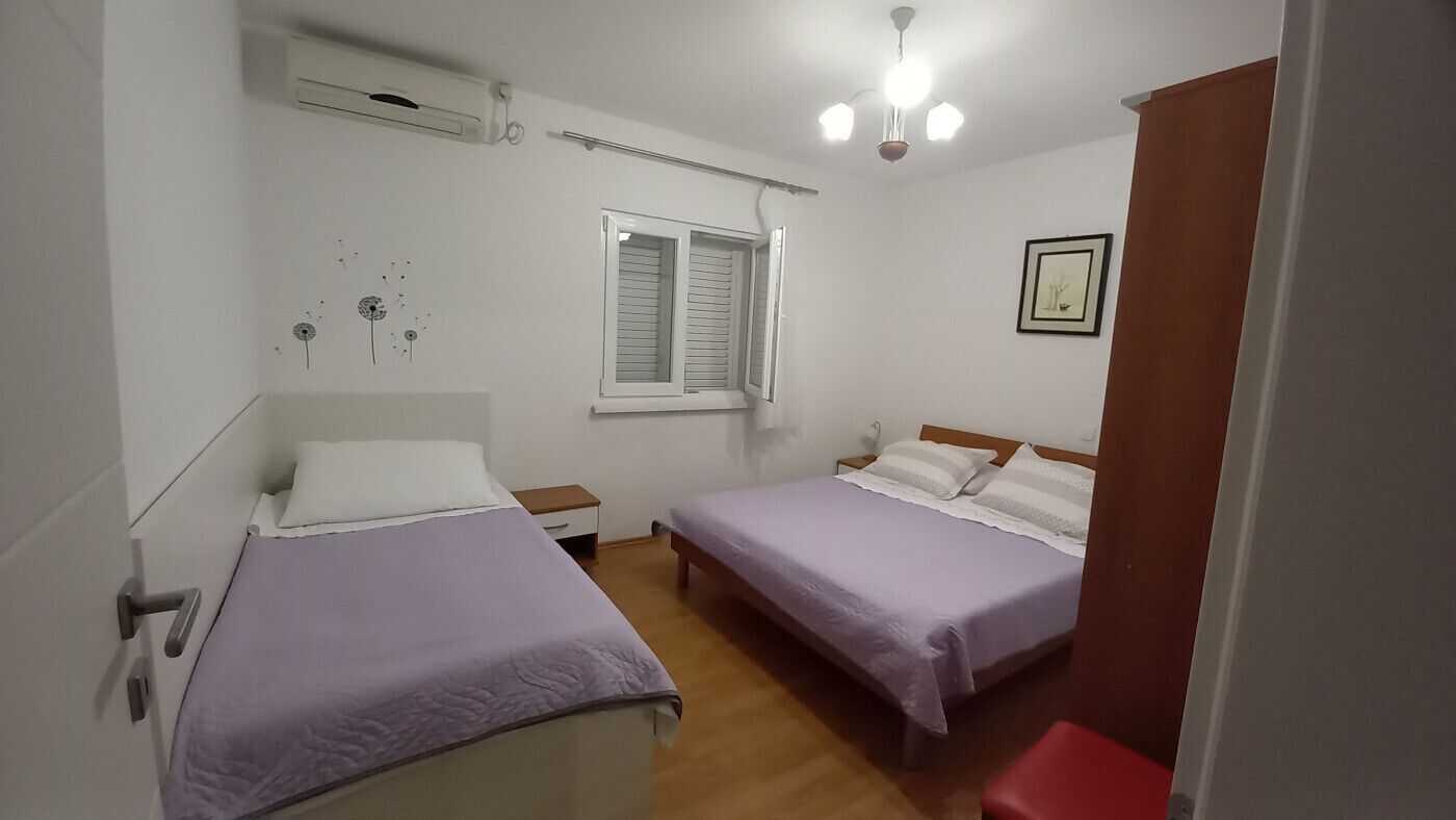 Quarto com duas camas, uma janela, uma luminária no teto e um ar condicionado fixado na parede.