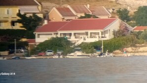 Une maison avec un toit rouge, un balcon et un bateau amarré dans l’eau.