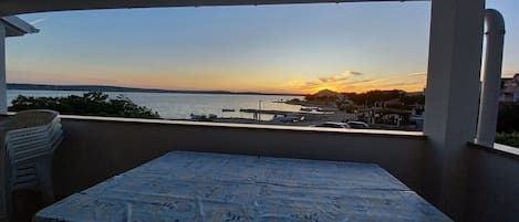 A balcony with a table and chairs, overlooking a marina with boats and a sunset view.