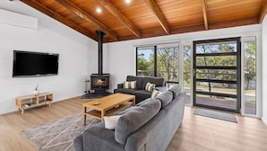 A modern living room with a large gray sectional sofa, a wooden coffee table, a black fireplace, and a flat-screen TV mounted on the wall.