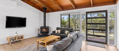 A modern living room with a large gray sectional sofa, a wooden coffee table, a black fireplace, and a flat-screen TV mounted on the wall.